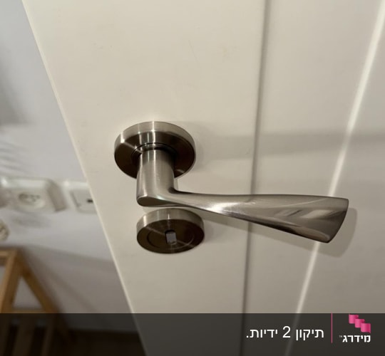 ידית דלת מתכתית על דלת לבנה
